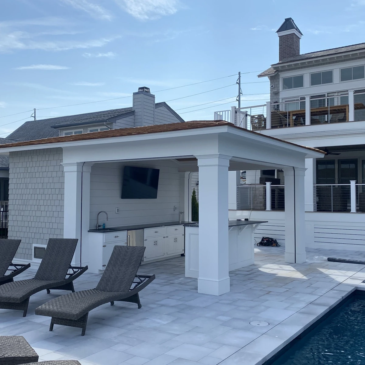 Poolside outdoor kitchen pavilion with white columns and lounge seating